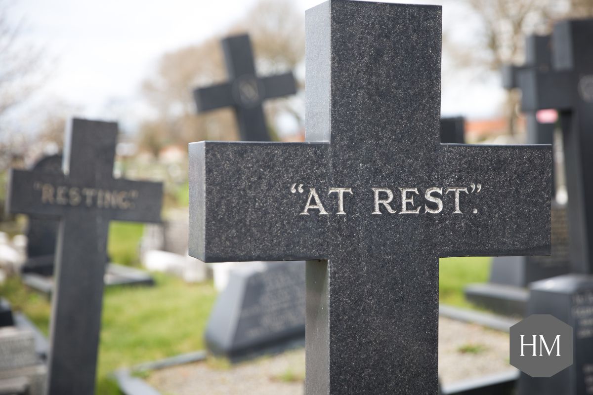 Stone cross in cemetery with "at rest" written on it