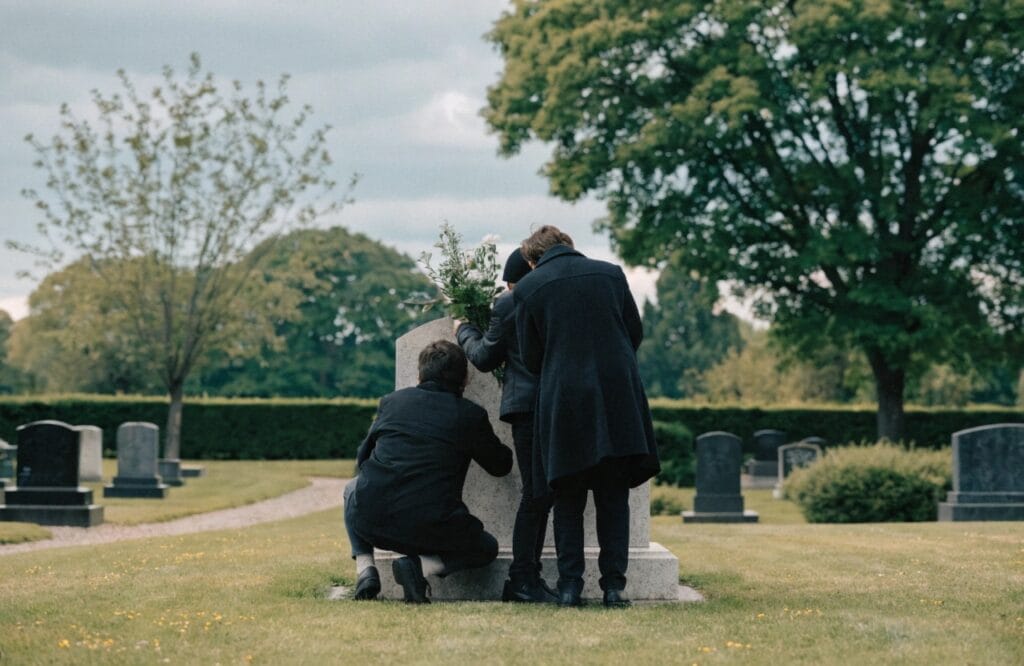 family placing flowers at a gravestone in a peaceful cemetery, seen from behind
